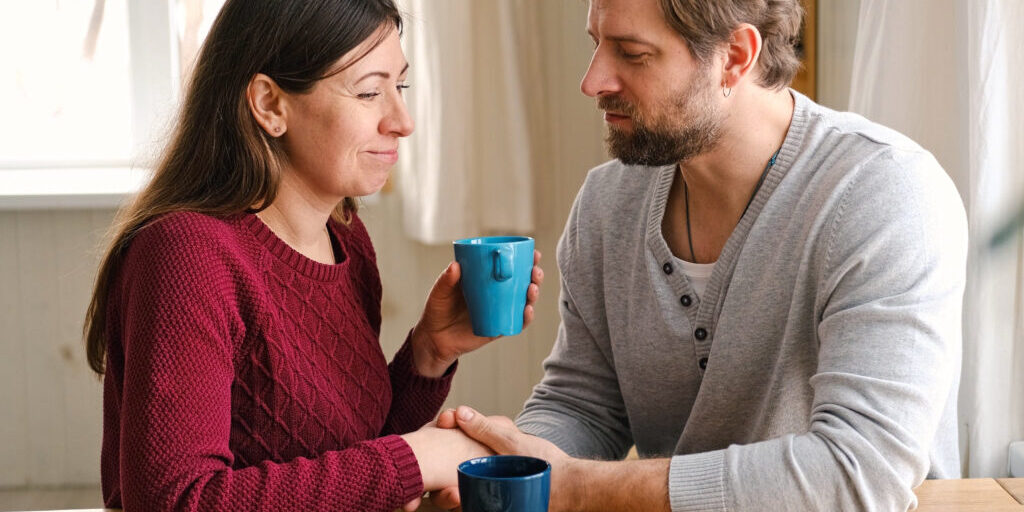 Loving mature couple interactions at home. Husband and wife hugging, holding hands and drinking morning coffee together. Man and woman talk about plans for weekend. Natural lighting. Intimate moments.